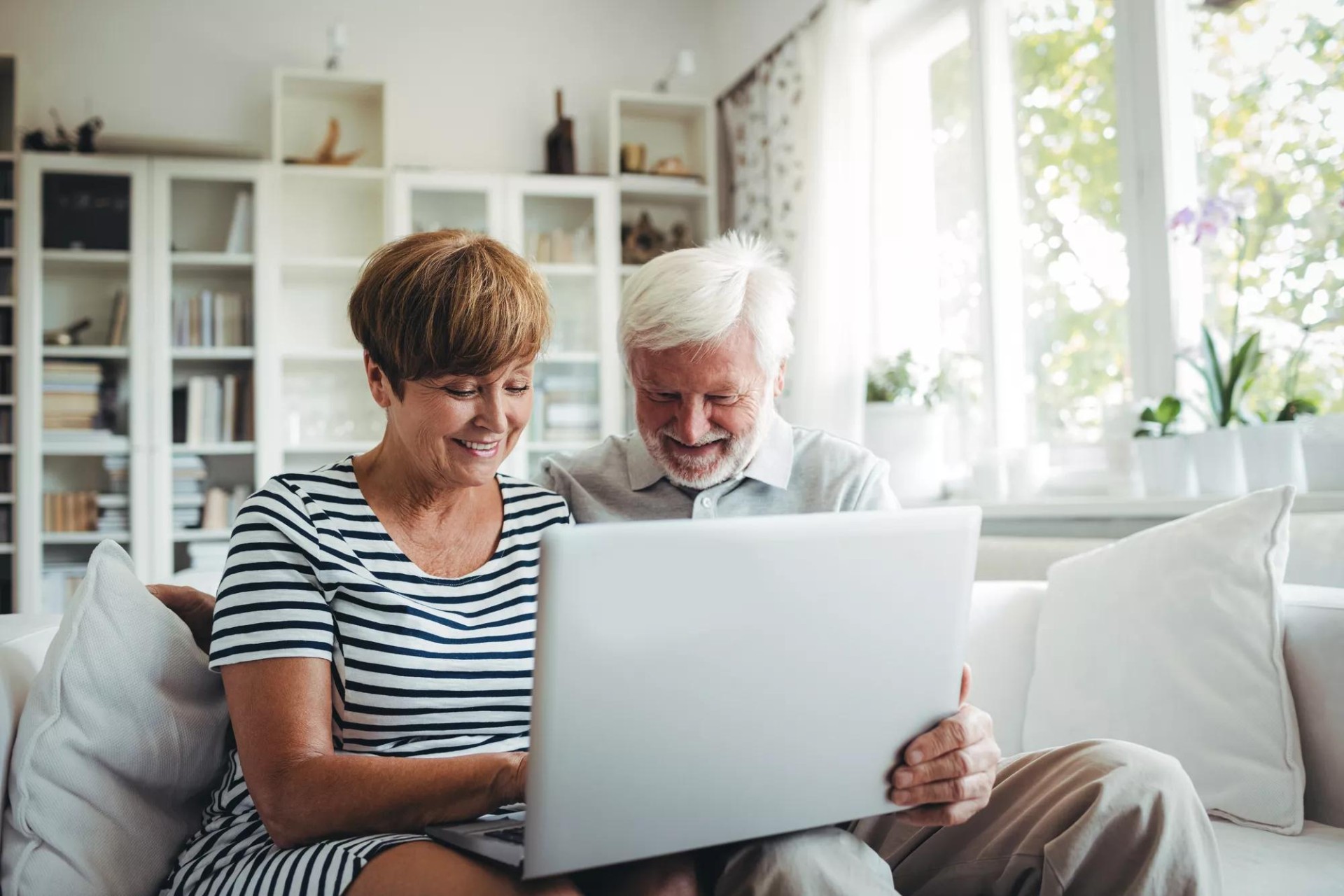 Senior couple is happily smiling while sitting on their living room sofa and looking at a computer screen. Senior couple is happily smiling while sitting on their living room sofa and looking at a computer screen.